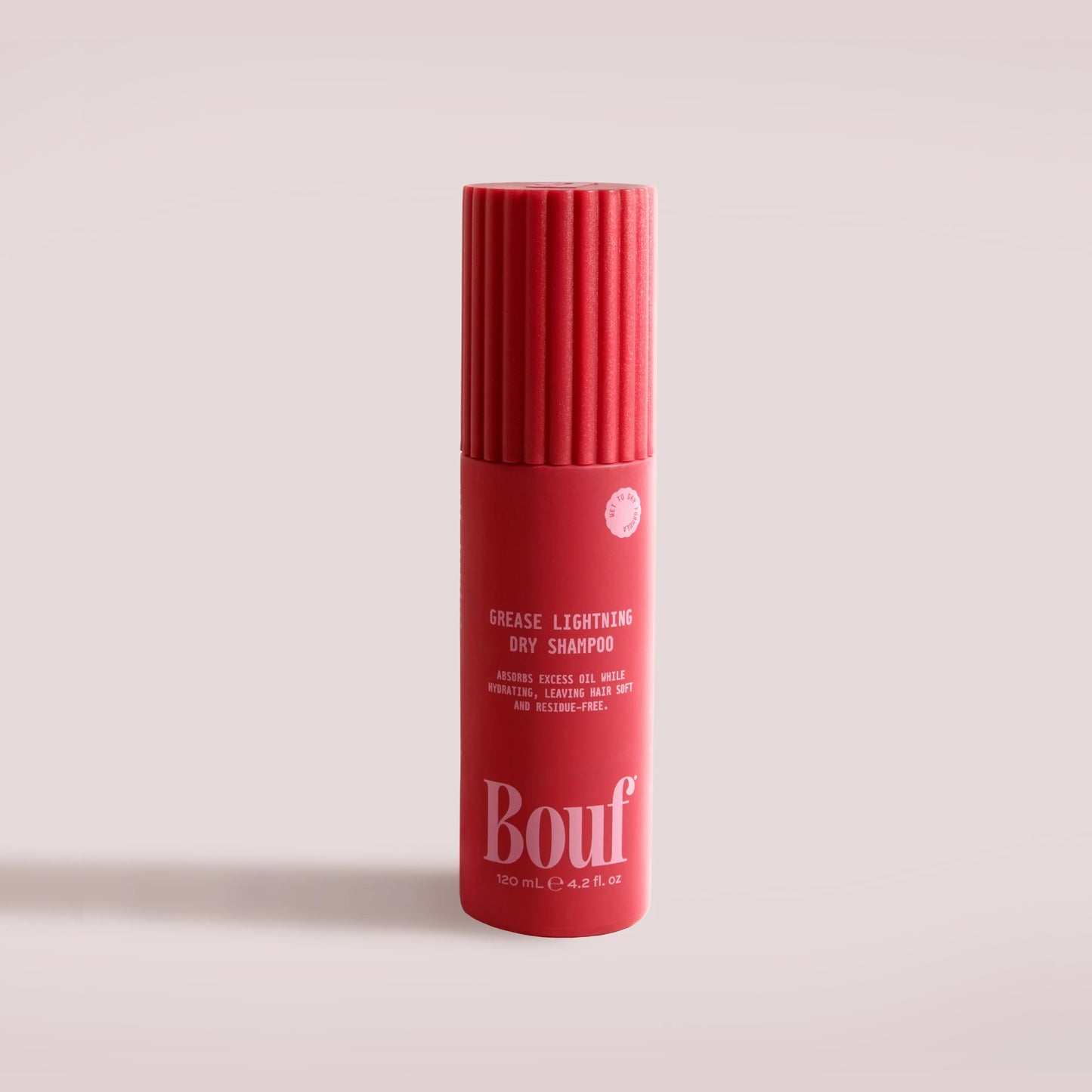 A red cylindrical bottle of Bouf Grease Lightening Dry Shampoo, featuring a ribbed cap and white text, set against a solid pale pink background.
