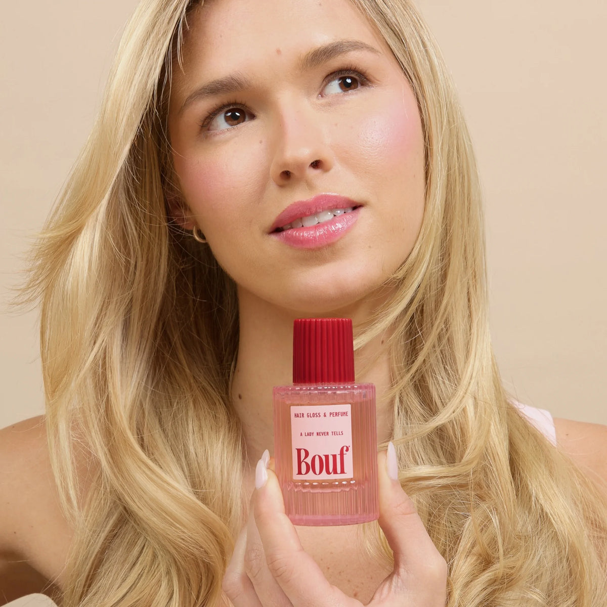 A blonde woman holds Bouf Hair Gloss & Perfume against a soft beige background.