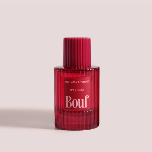 A ribbed glass bottle of Bouf Hair Gloss & Perfume in the scent, It's A Secret set against a solid pale grey background.