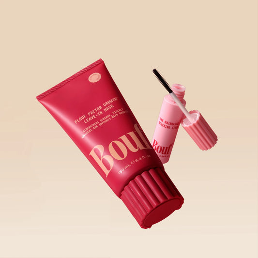 The Flouf Factor Growth Leave-In Mask and the Hairmaster Slicking Stick from Bouf's Slick Me Baby Bundle, shown together on a beige background — a red squeeze tube and a pink applicator wand with its cap removed