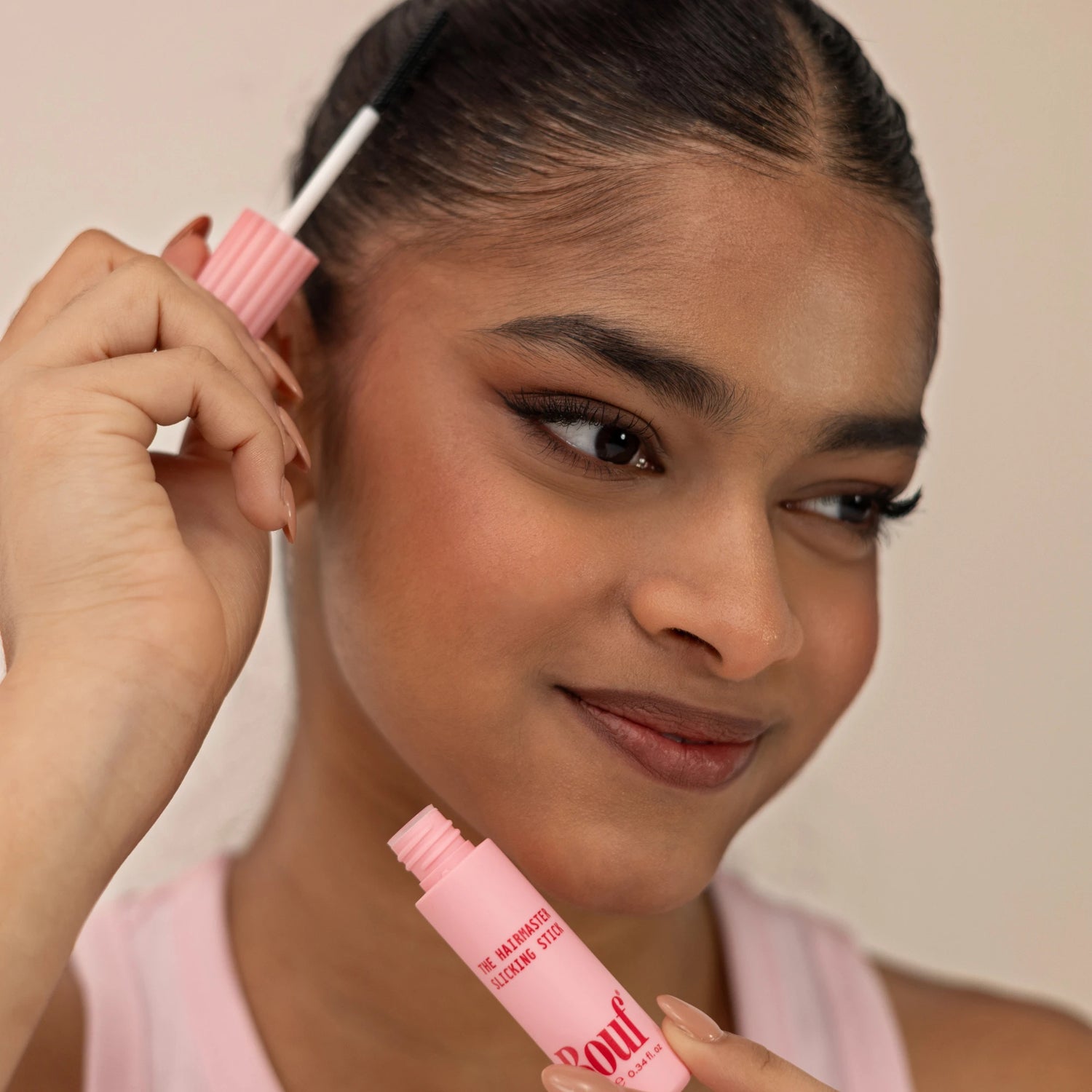 A close-up of a woman applying the Hairmaster Slicking Stick from Bouf.