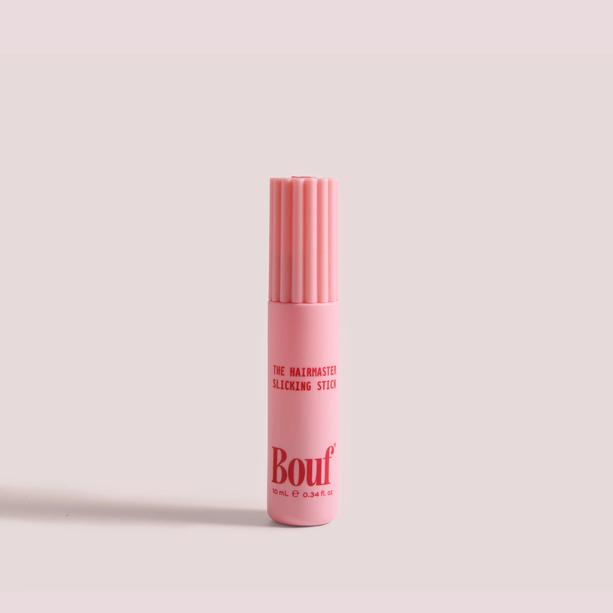 The Hairmaster Slicking Stick by Bouf, standing upright on a plain light pink background.