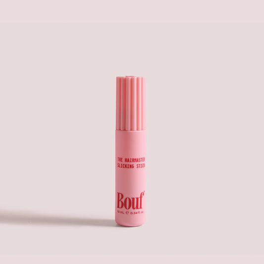 The Hairmaster Slicking Stick by Bouf, standing upright on a plain light pink background.