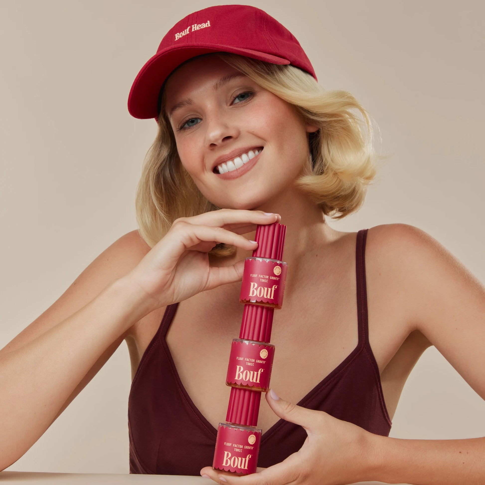 Woman holding a stack of 'Bouf' nail polish bottles against a beige background