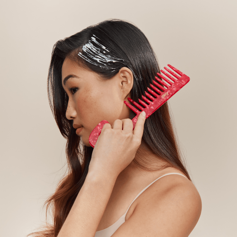 Woman applying hair mask with a red comb on a beige background